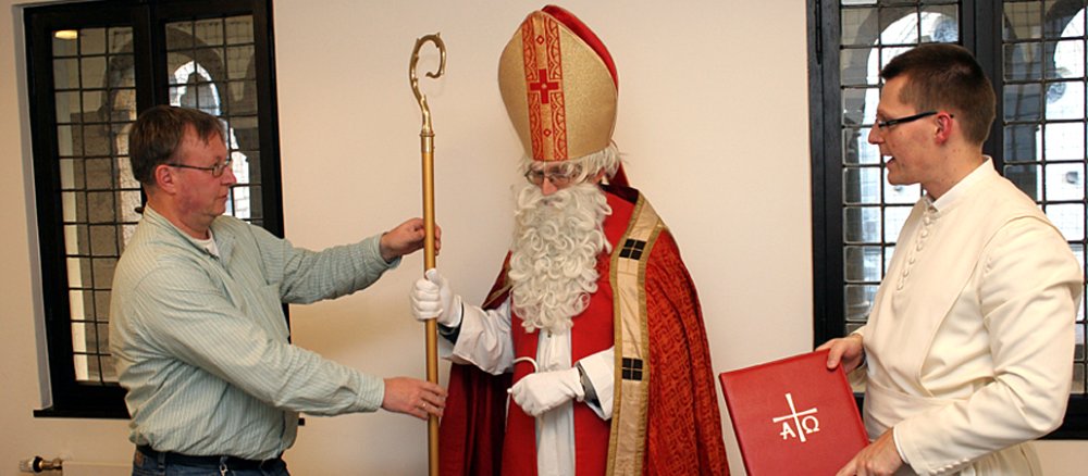 Der Teilnehmer an der Nikolaus-Fortbildung Christoph Büser wird mit Mitra, Stab und Bischofsmantel eingekleidet.