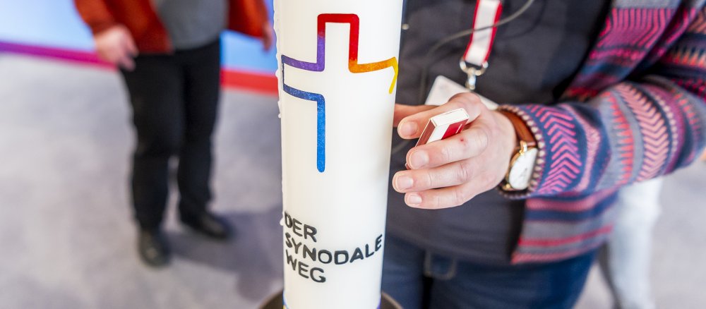 Eine Kerze mit dem Logo des Synodalen Wegs wird entzündet