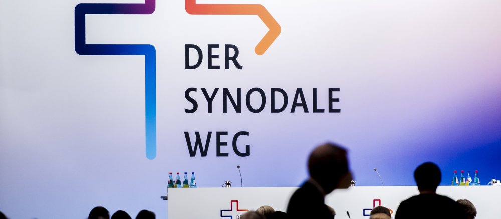 Schattenhafte Umrisse vor dem Logo des Synodalen Wegs