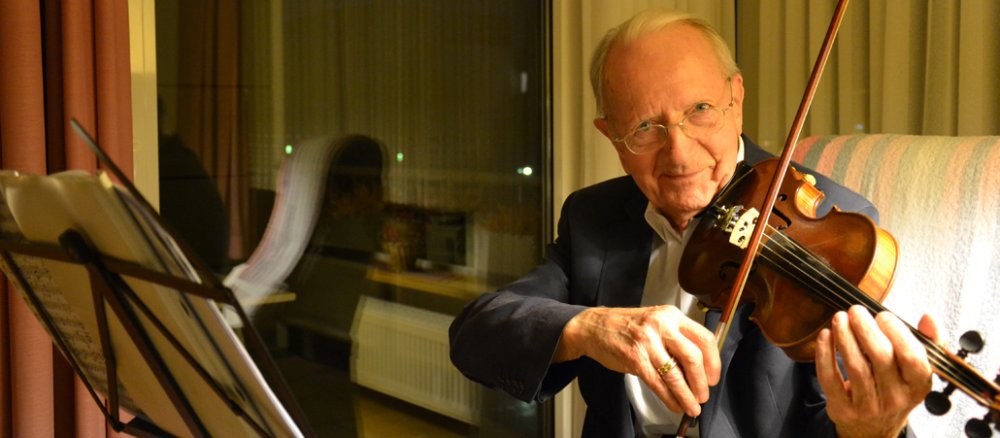 Alter Herr sitzt aufrecht im Sessel und spielt Geige